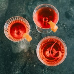 three red cocktails with orange peels in different crystal glasses